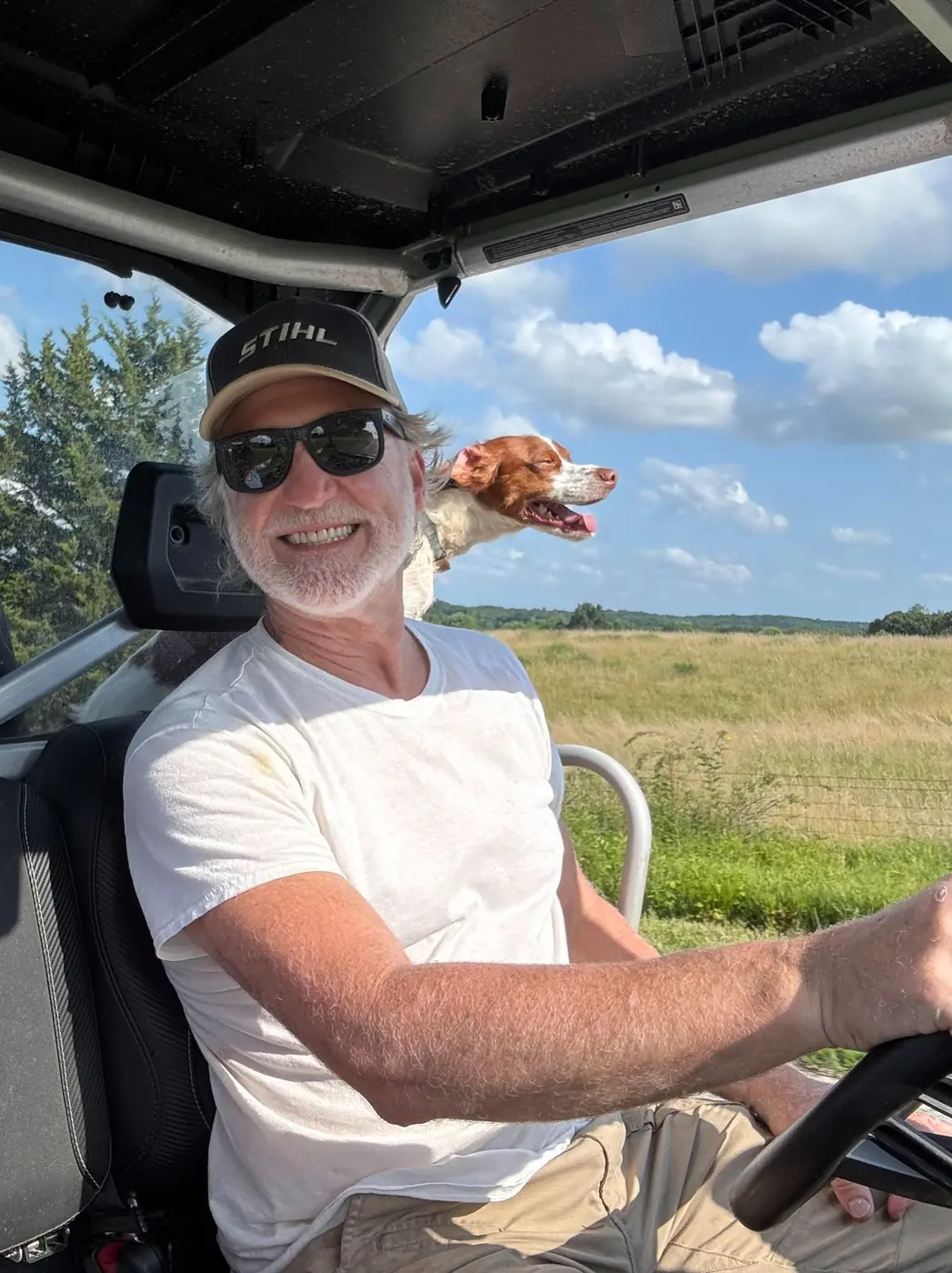 Clark Colwell at the wheel of a utility vehicle, his bird dog over his shoulder.